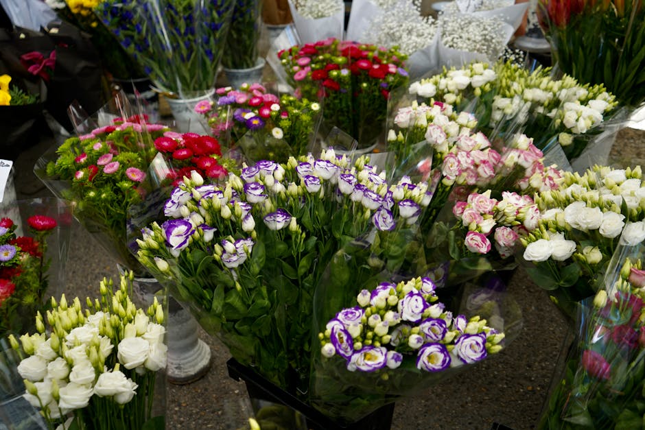 A vibrant display of freshly cut flowers arranged in bouquets at a flower shop. The arrangement includes purple and white lisianthus, white roses, pink and white ranunculus, and red and pink anemones,