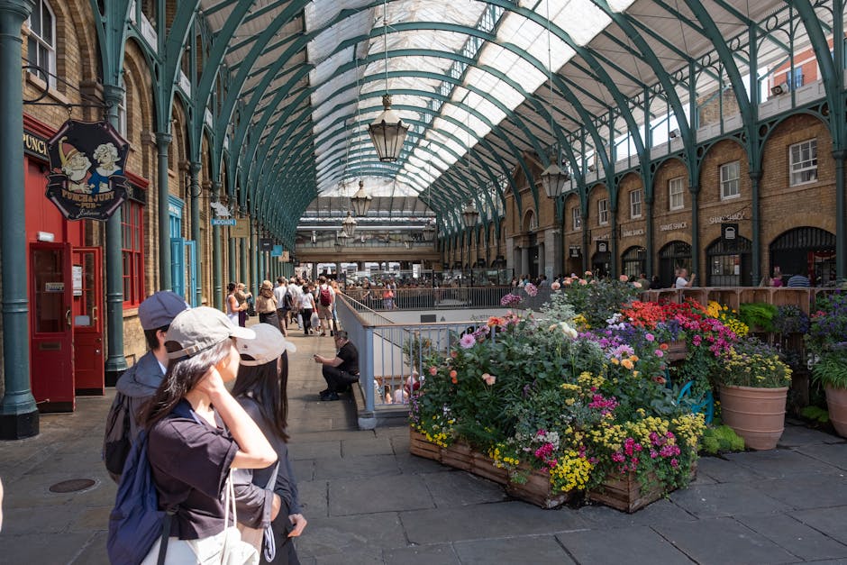 Inside the historic Victorian market building with a glass and metal arched ceiling, a floral display features a vibrant bouquet of fresh flowers including pink, purple, yellow, and white blooms arran